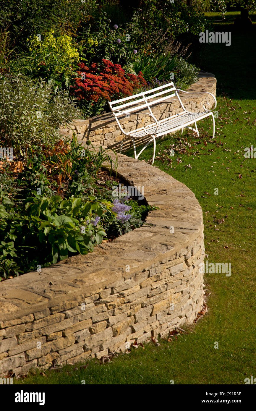 curved cotswold stone wall with raised flower bed in english garden